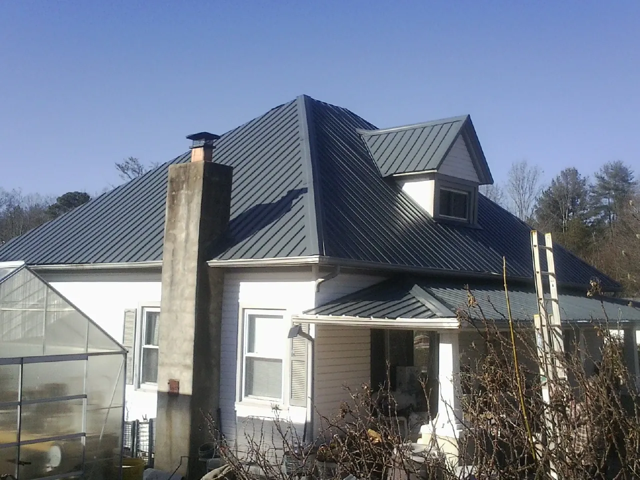 Dark blue standing seam metal roof on a white farmhouse with dormer — Slate & Tile Roof Repair by Roofing Brothers in Breezewood