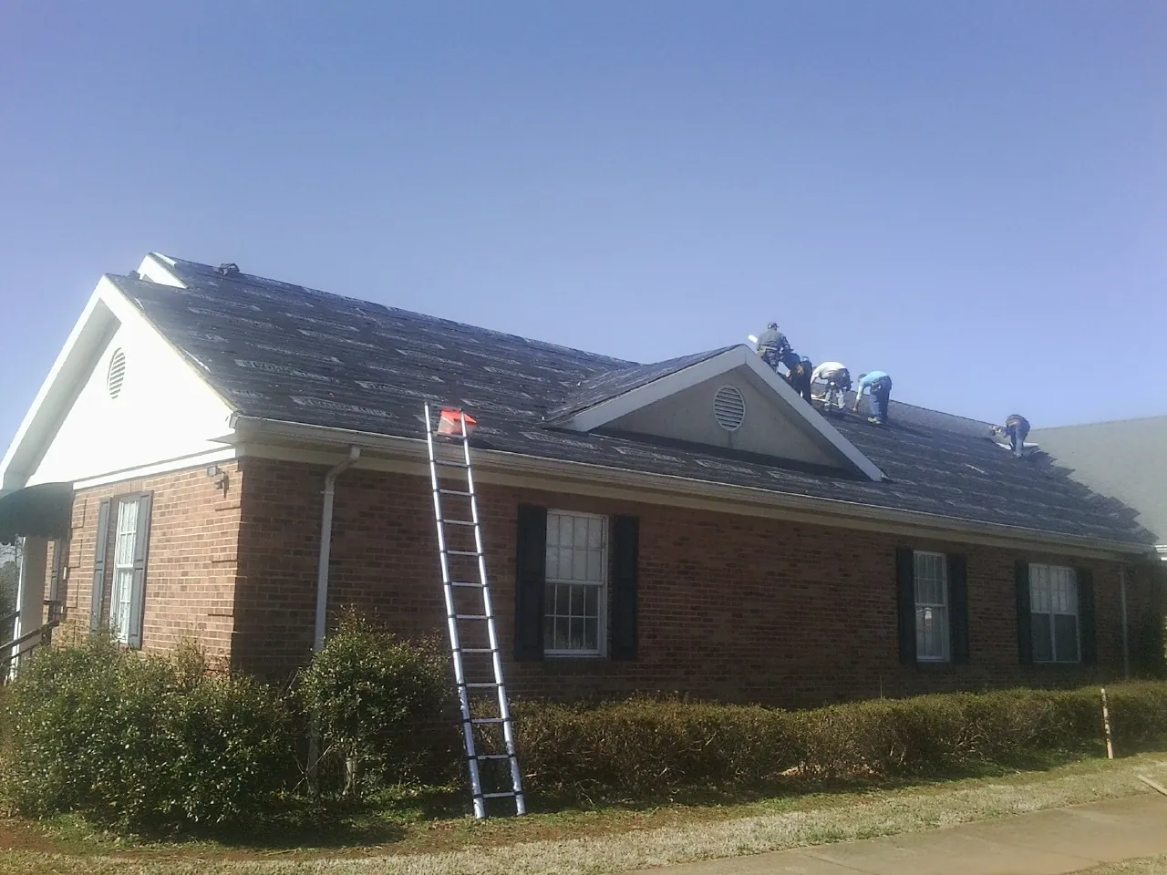 Crew tearing shingles off a brick ranch roof with a ladder set — Metal Roof Repair work by our crew in Breezewood