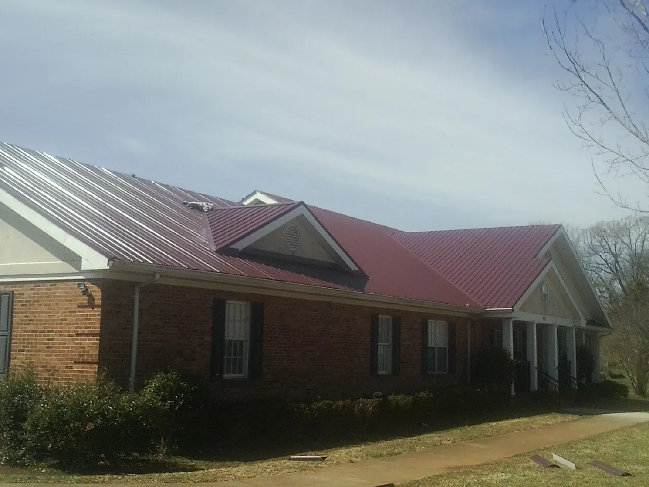 Red metal roof with gabled entries on a long brick building, from a Hail Damage Roof Repair job in Breezewood