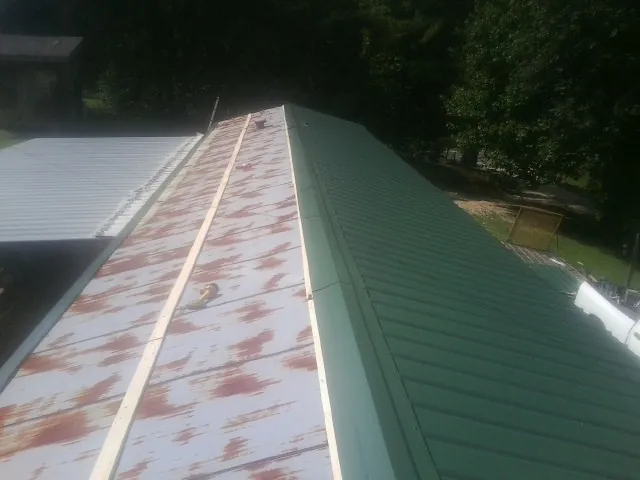 Old rusted panels beside newly installed green metal roofing — Wind Damage Roof Repair by Roofing Brothers in Breezewood