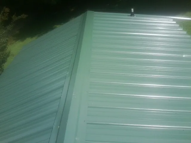 New green metal panels meeting at the ridge of a roof — Flat Roof Repair work by our crew in Breezewood