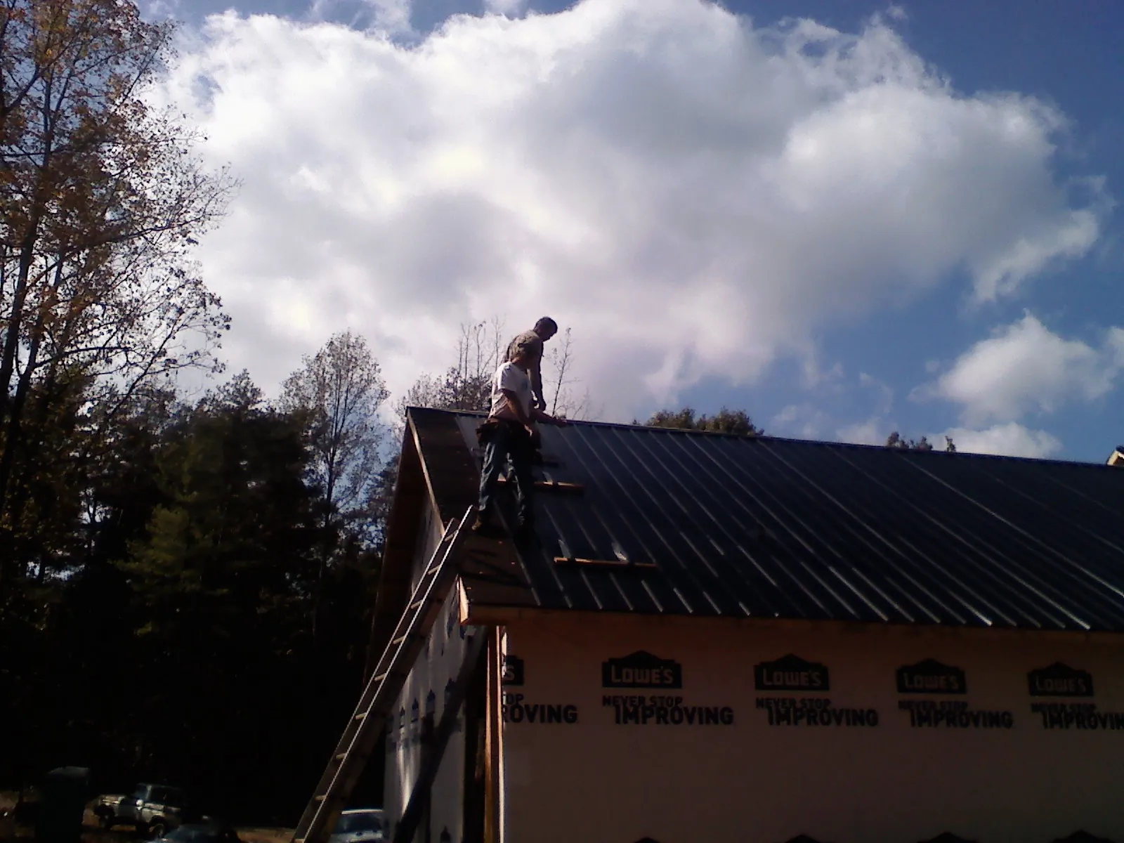 Roofer fastening dark metal panels high against a cloudy sky, from a Roof Inspection job in Breezewood