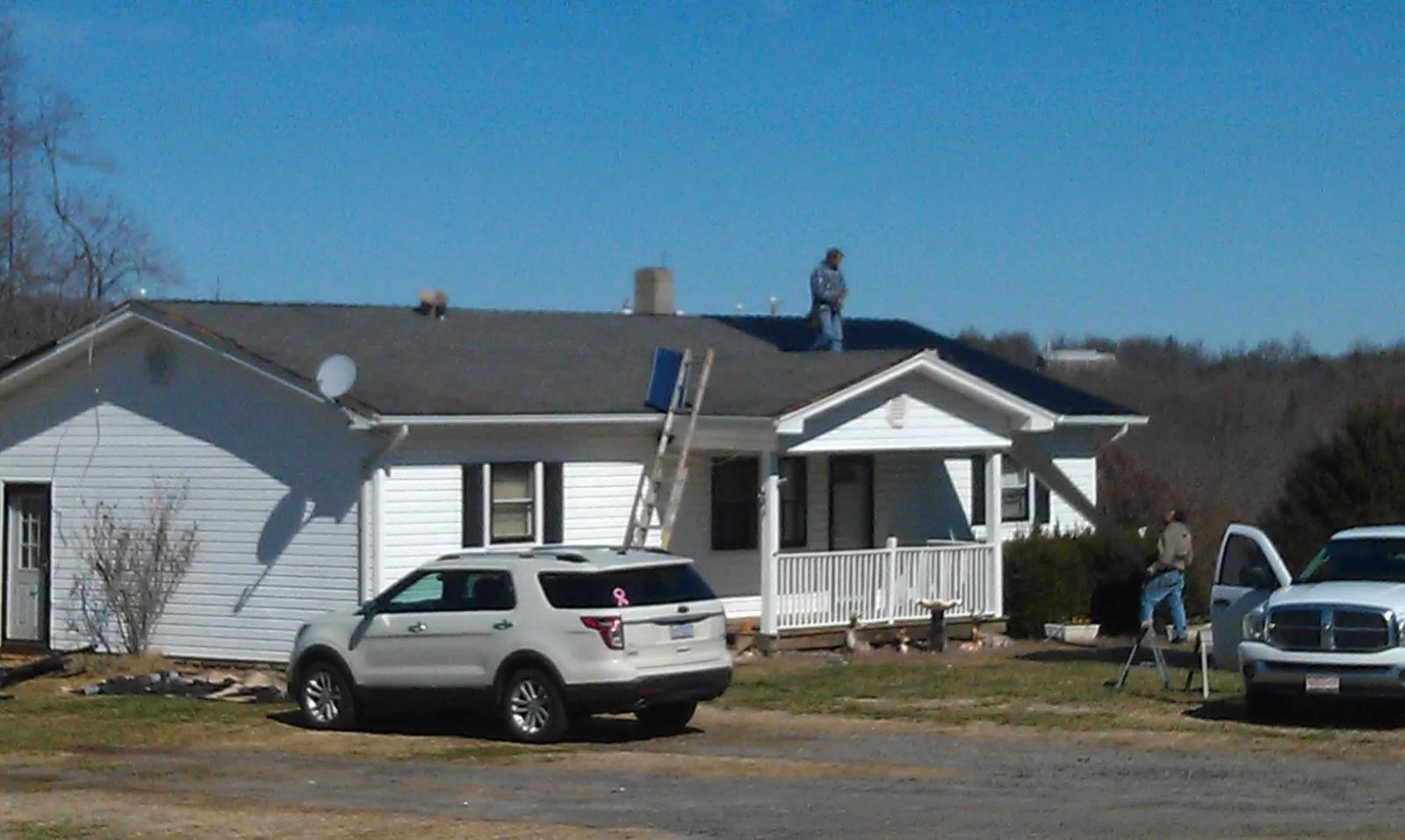 Roofers stripping shingles from a white ranch house roof in Breezewood