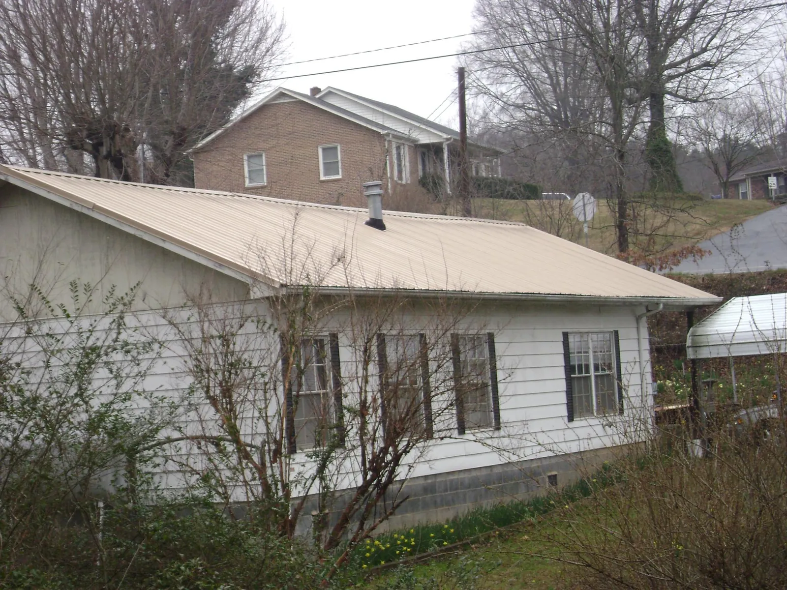 Tan metal roof on a white sided house set into a hillside — Commercial Roofing by Roofing Brothers in Breezewood