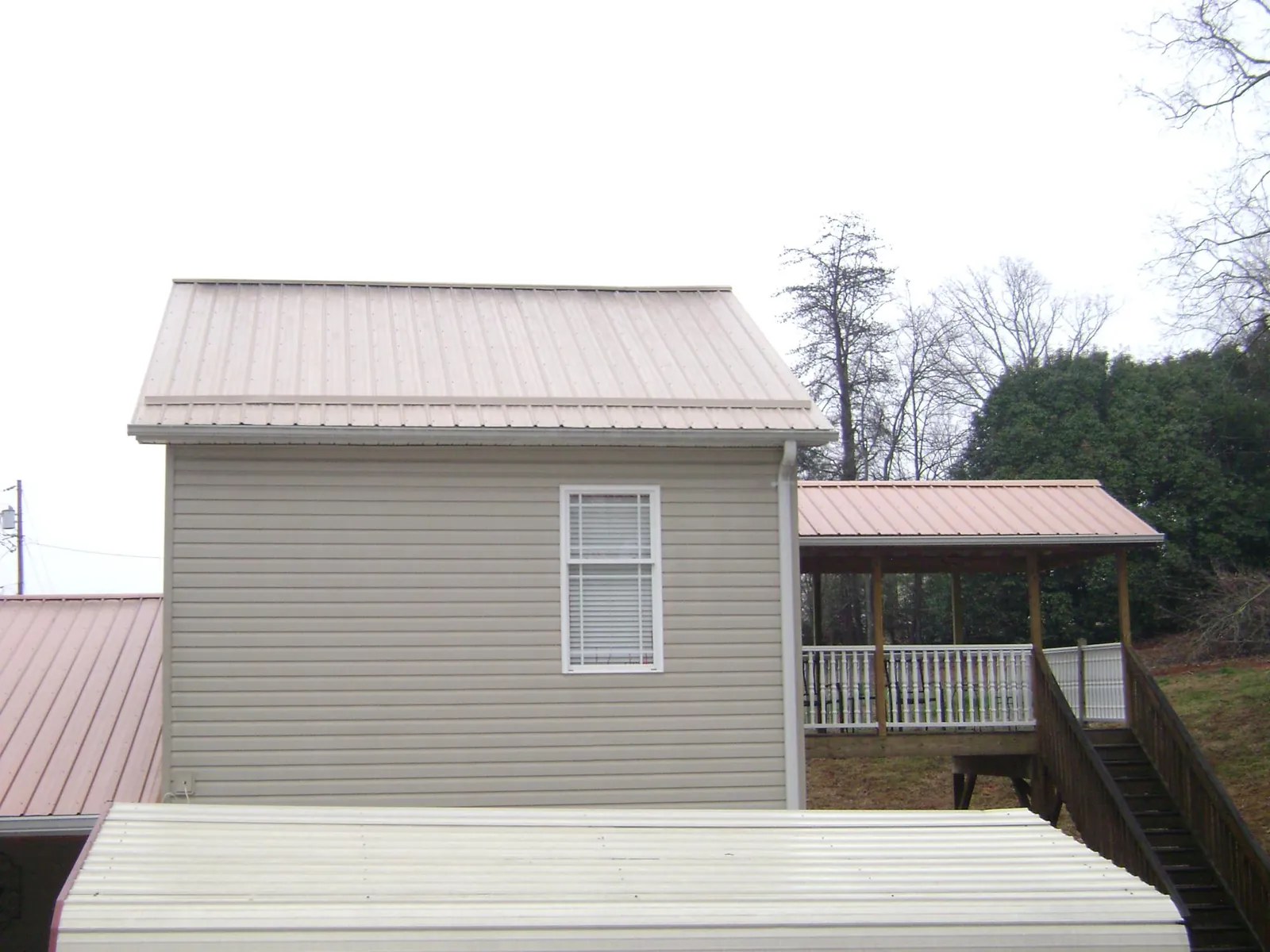 Tan metal roofs on a two story addition and attached porch, from a Roof Replacement job in Breezewood